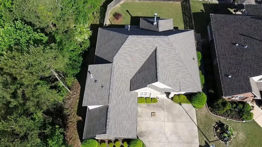 Overhead drone view of a home with gray architectural shingle roof, concrete driveway, and trees in Fultondale, AL