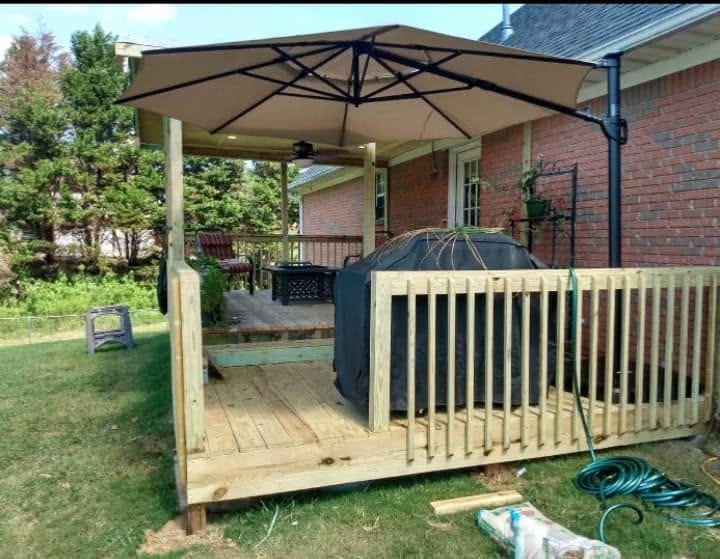 New pressure-treated wood deck with railing, tan cantilever umbrella, and covered grill behind a brick home.