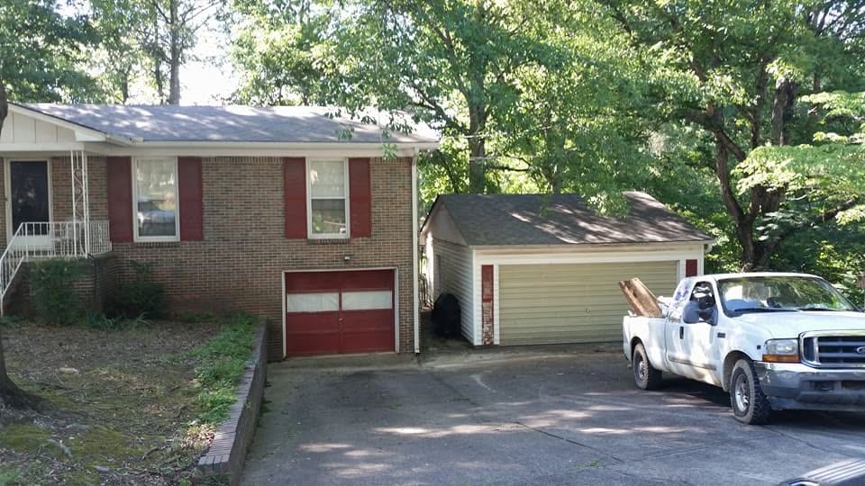 Brick split-level house with red shutters beside a detached garage with new gray shingle roof and a white work truck in the