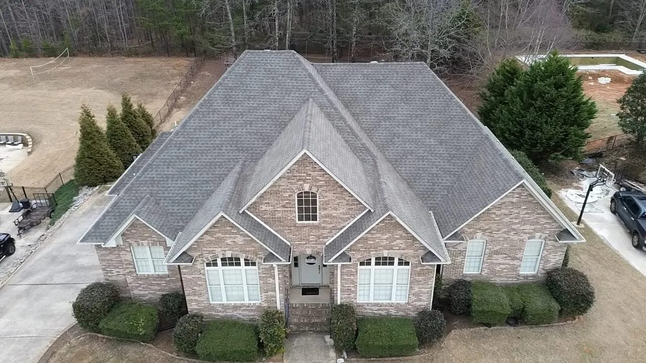 Aerial drone view of a large brick home with three front gables and a gray architectural shingle roof.