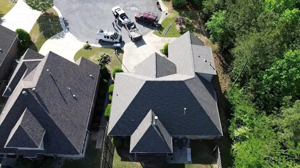 Aerial view of a house with a gray hip roof on a cul-de-sac, with work trucks and ladders parked in the street