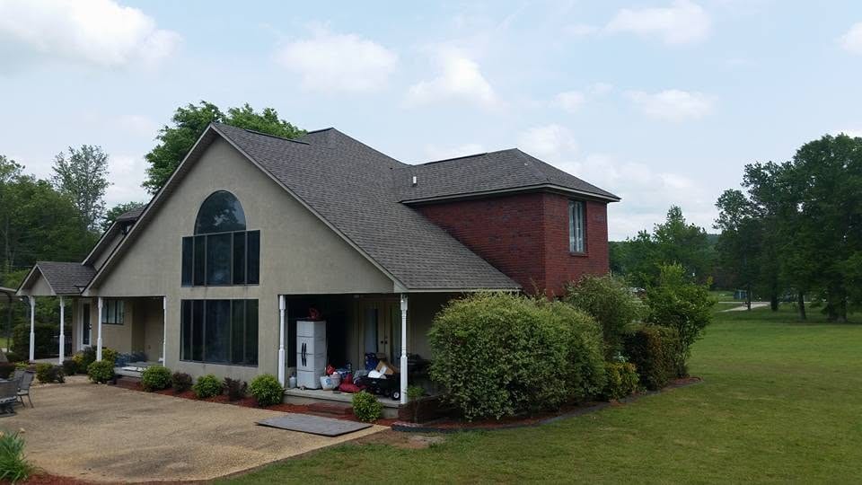 Two-story stucco home with brick upper section, gray architectural shingle roof, arched window wall, and covered porch on a