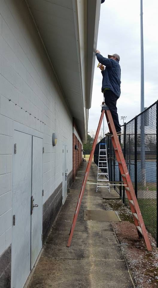 Worker on an orange extension ladder repairing a gutter along the eave of a concrete block commercial building.
